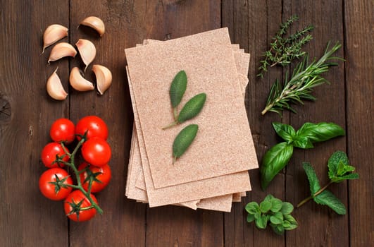 Whole wheat lasagna sheets, tomatoes, garlic and herbs on wooden background