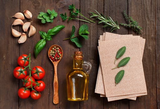 Whole wheat lasagna sheets, tomatoes, garlic, olive oil and herbs on wooden background