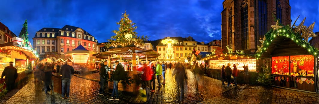 Christmas market in Heidelberg,Germany,a panorama shot at dusk showing illuminated kiosks,architecture and blurred people
