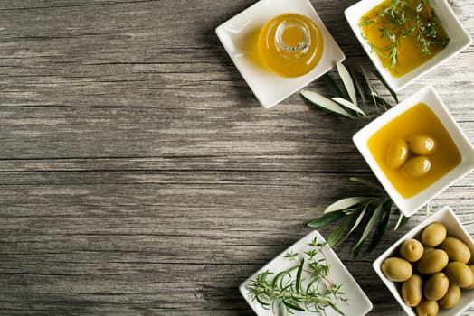 Olive oil with fresh herbs on wooden background