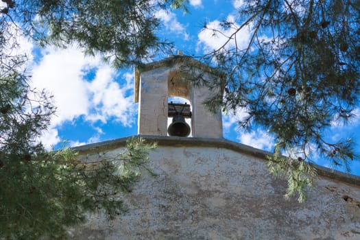 Church tower with bell in Spanish style against a blue sky.