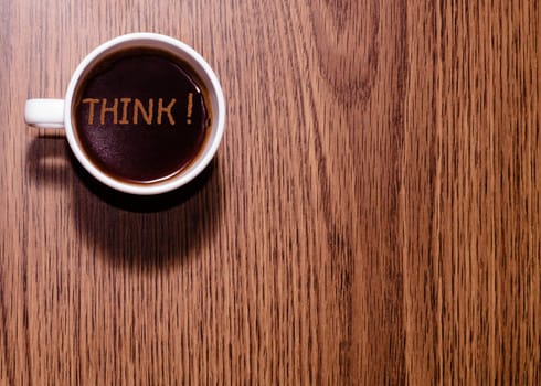 Inscription Think and cup of coffee on wooden table
