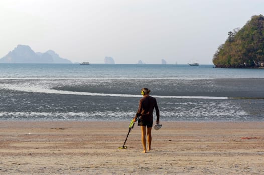 a treasure hunter with Metal detector on sunrise on the beach