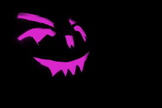 purple carved face of pumpkin glowing on halloween black background