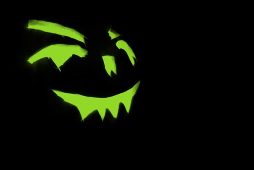 green carved face of pumpkin glowing on halloween black background