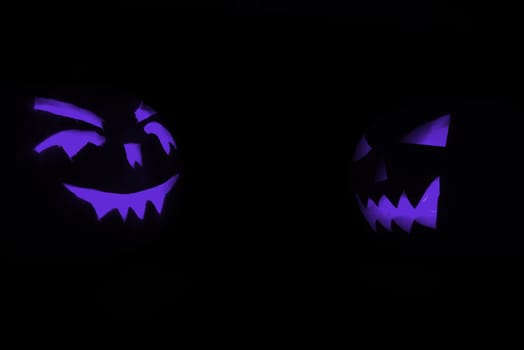 two blue carved face of pumpkin glowing on halloween black background