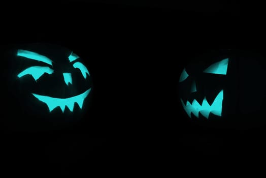 two blue carved face of pumpkin glowing on halloween black background