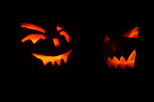 two carved face of pumpkin glowing on halloween black background