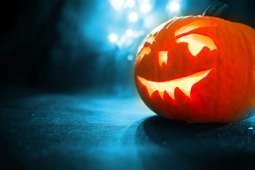 carved face of pumpkin glowing on a blue background bokeh light background