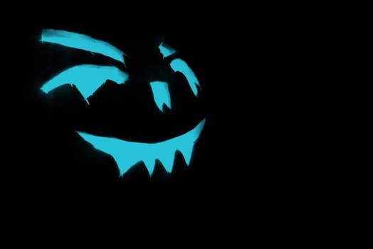 blue carved face of pumpkin glowing on halloween black background