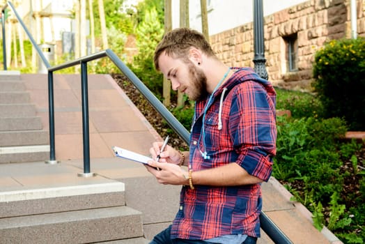 young man bearded standing by stairs with clipboard and writing