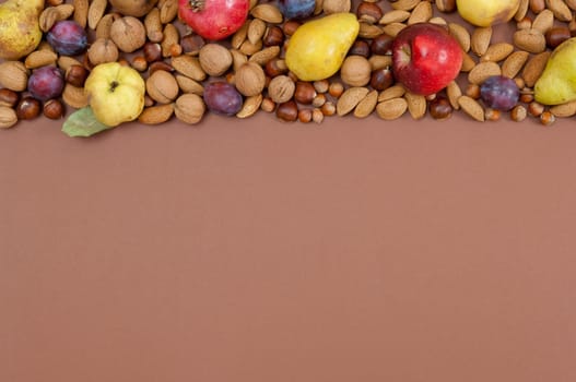 Organic autumn fruits and nuts on brown background with copy space
