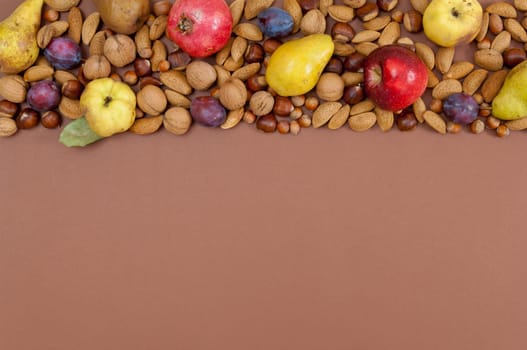 Organic autumn fruits and nuts on brown background with copy space