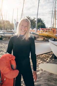 Portrait of a senior woman standing in a boat bay. She is wearing a wetsuit and holding a lifejacket.