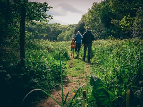 Father, mother and daughter walking through the woodlands together. They are all using sticks as walking aid.