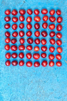 Square arrangement of ripe cherries on blue textrured background, cherry pattern