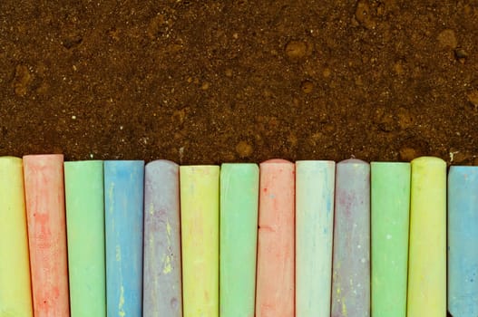 Colorful pastel sidewalk chalk on dark asphalt background. Top view