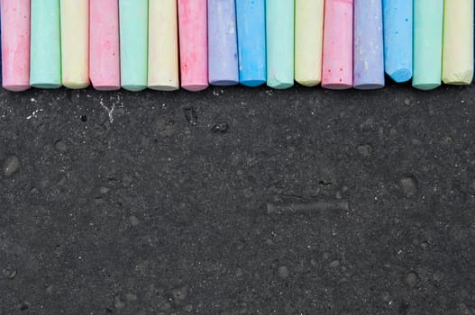 Colorful pastel sidewalk chalk on dark asphalt background. Top view