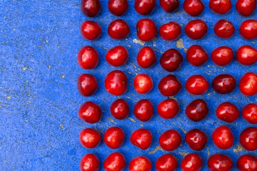 Square arrangement of ripe cherries on blue textrured background, cherry pattern