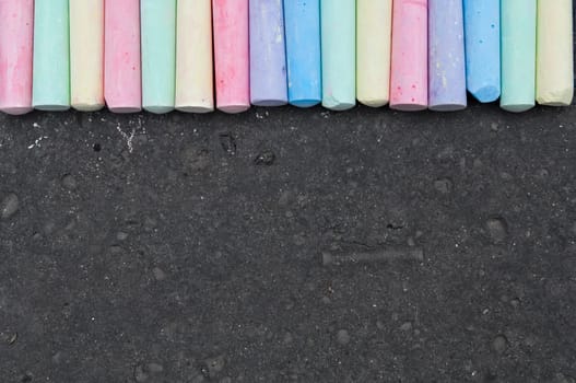 Colorful pastel sidewalk chalk on dark asphalt background. Top view