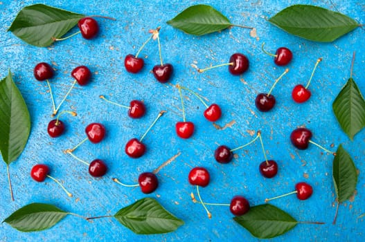 Cherry, cherries with cherry leaves on textured light blue background, top view