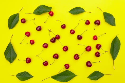 Cherry, cherries with cherry leaves on yellow background, top view