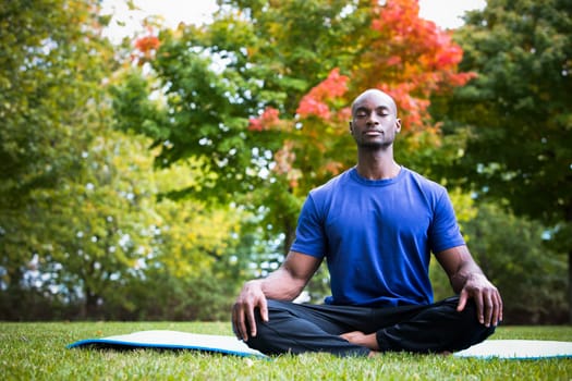 young black man wearing athletic wear sitting in the park exercising yoga