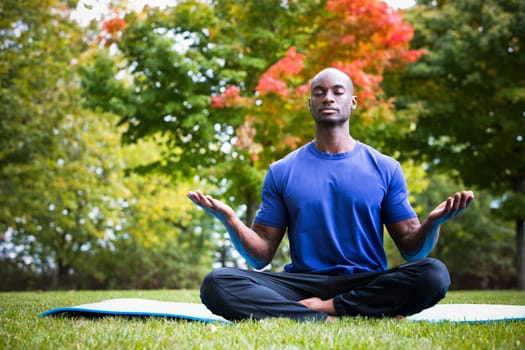 young black man wearing athletic wear sitting in the park exercising yoga