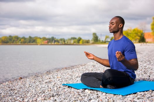 young black man wearing athletic wear sitting on the beach exercising yoga