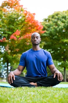 young black man wearing athletic wear sitting in the park exercising yoga