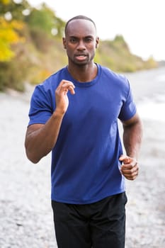 young black man wearing athletic wear running on the beach