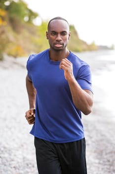 young black man wearing athletic wear running on the beach