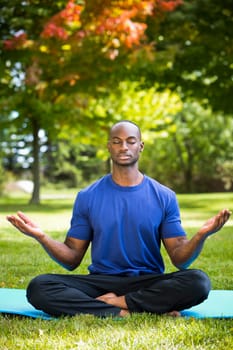 young black man wearing athletic wear sitting in the park exercising yoga