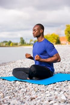 young black man wearing athletic wear sitting on the beach exercising yoga
