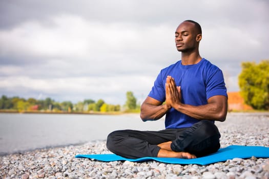 young black man wearing athletic wear sitting on the beach exercising yoga