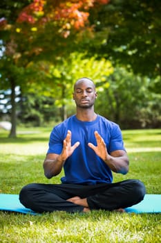 young black man wearing athletic wear sitting in the park exercising yoga