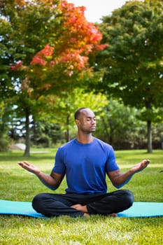 young black man wearing athletic wear sitting in the park exercising yoga
