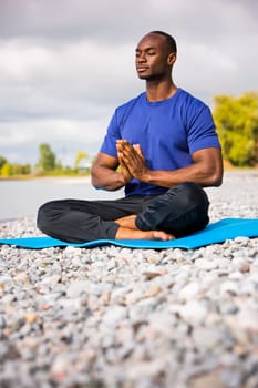 young black man wearing athletic wear sitting on the beach exercising yoga