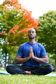 young black man wearing athletic wear sitting in the park exercising yoga