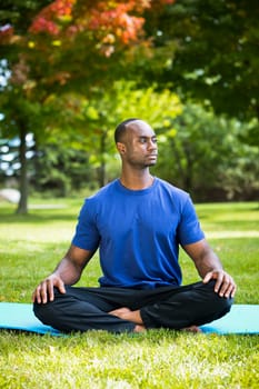 young black man wearing athletic wear sitting in the park exercising yoga