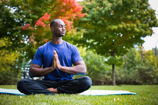 young black man wearing athletic wear sitting in the park exercising yoga