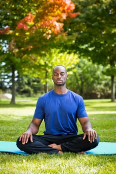 young black man wearing athletic wear sitting in the park exercising yoga