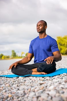 young black man wearing athletic wear sitting on the beach exercising yoga