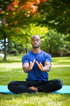 young black man wearing athletic wear sitting in the park exercising yoga