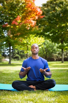 young black man wearing athletic wear sitting in the park exercising yoga
