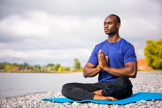 young black man wearing athletic wear sitting on the beach exercising yoga