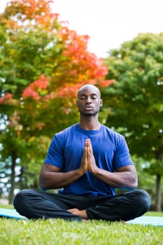 young black man wearing athletic wear sitting in the park exercising yoga