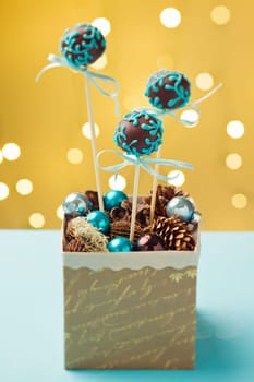 Chocolate cake pops garnished with turquoise icing sticking in nice Christmas gift box. Very shallow depth of field with Christmas lights in the background