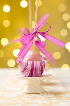 Pink Christmas cake pops sticking upside down in miniature cupcake liners. Very shallow depth of field with Christmas lights in the background