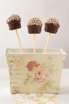Cupcake shaped cake pops made with chocolate and tiny little pearls as topping. They are sticking in a vintage gift box. Very shallow depth of field